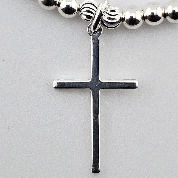 Close-up of sterling silver cross charm on bracelet.