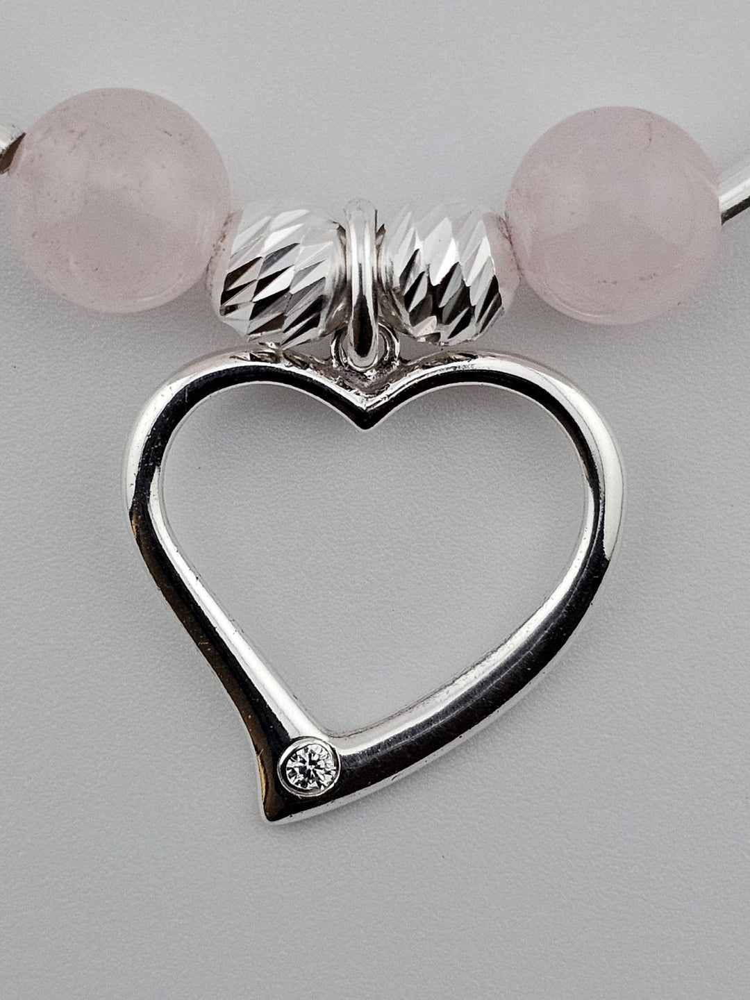 Close-up of sterling silver heart charm with single crystal detail on rose quartz bracelet.