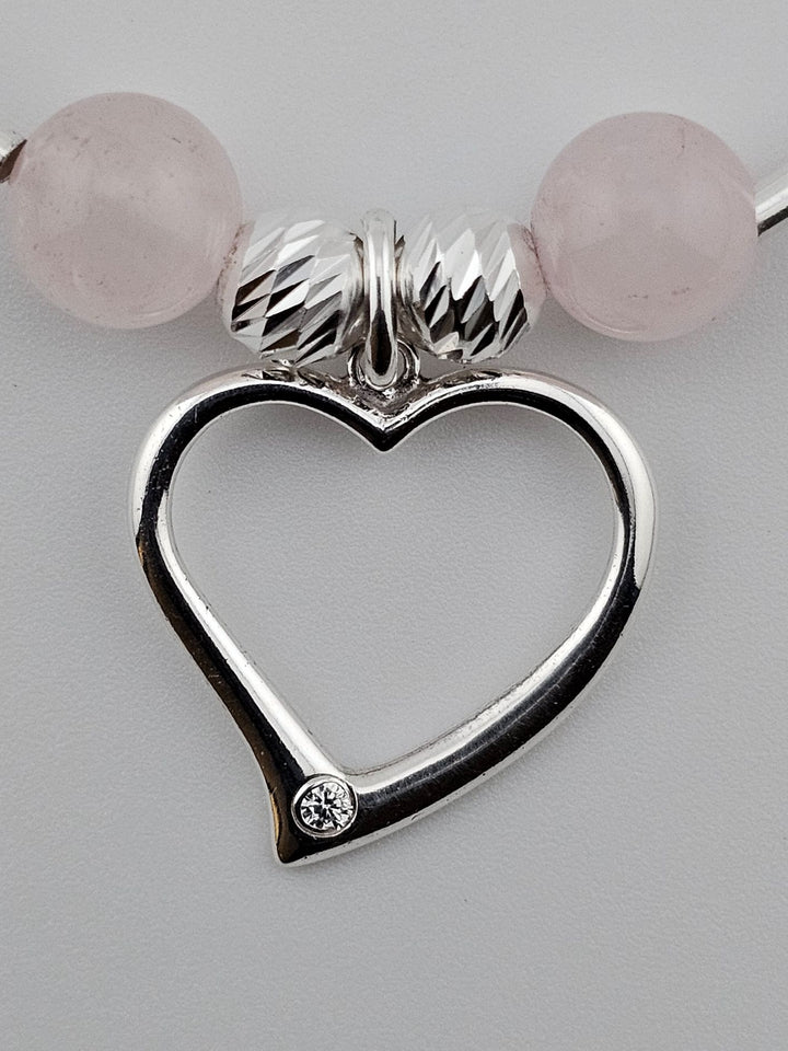 Close-up of sterling silver heart charm with single crystal detail on rose quartz bracelet.