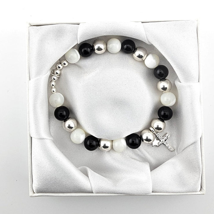 Top view of black and white gemstone bracelet with sterling silver cross and star charms in satin-lined box.