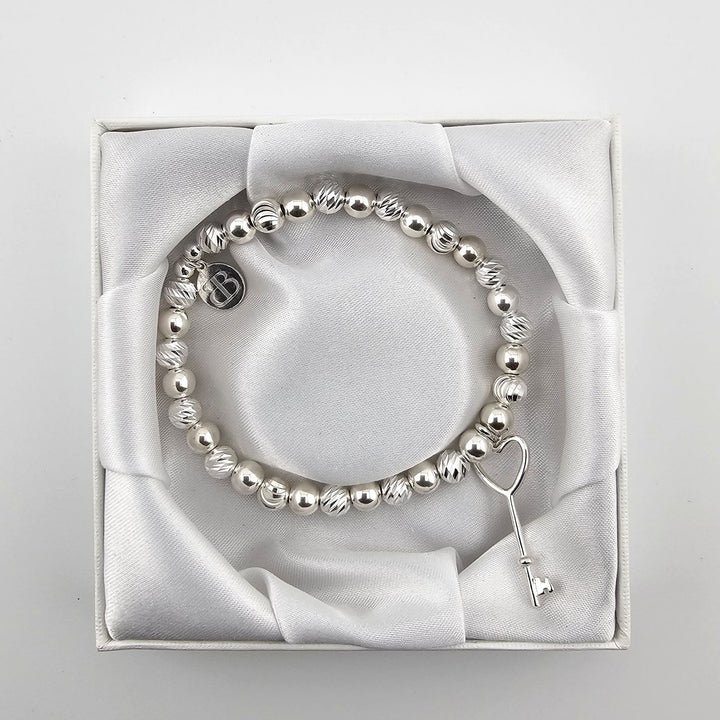 Top view of silver heart key bracelet in satin presentation box.