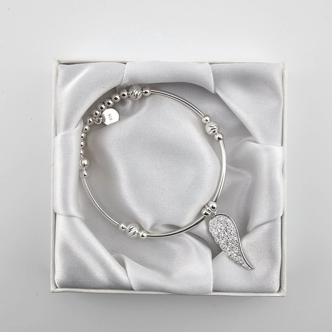 Top view of silver angel wing bracelet in satin-lined white box.