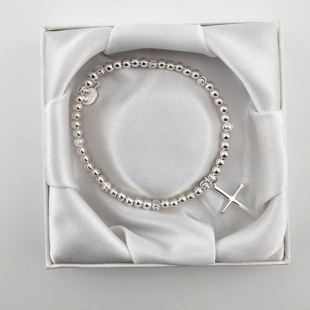 Top view of silver beaded bracelet with cross charm in satin-lined box.