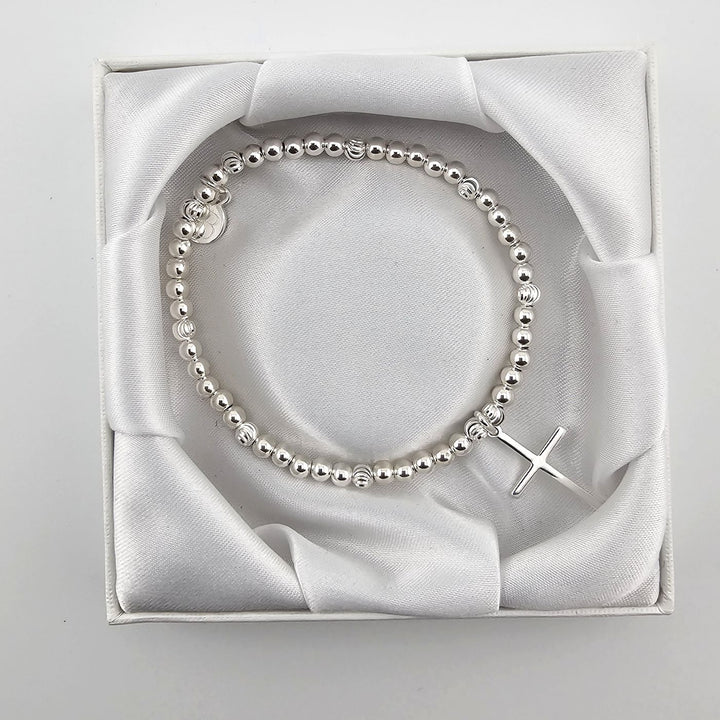 Top view of silver beaded bracelet with cross charm in satin-lined box.