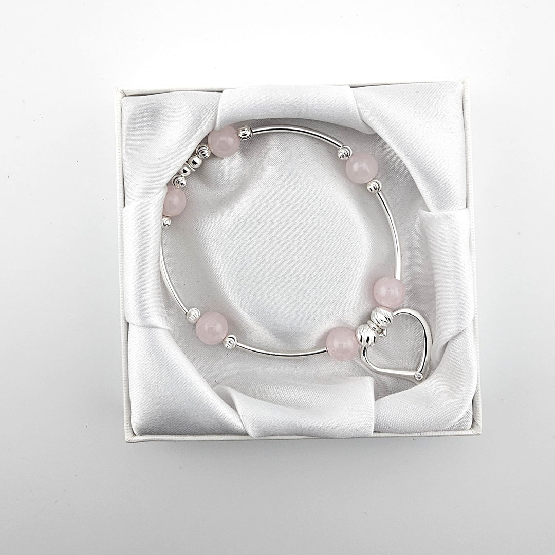 Top view of silver bracelet with rose quartz and heart charm in satin-lined box.