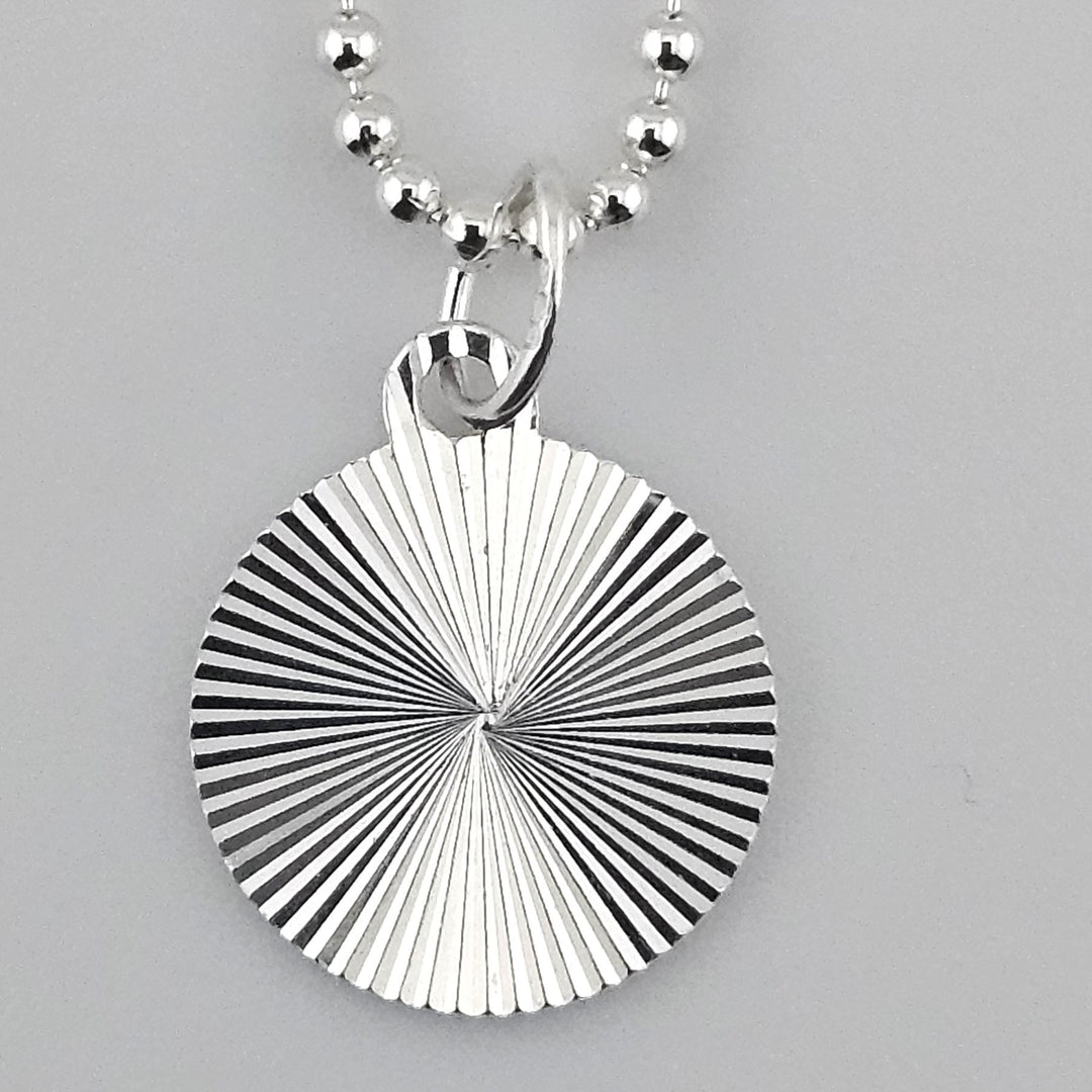 Close-up of 12mm starburst disc charm in 925 sterling silver with engraved radial design.