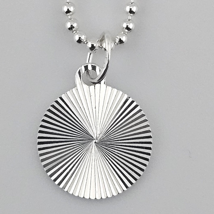 Close-up of 12mm starburst disc charm in 925 sterling silver with engraved radial design.