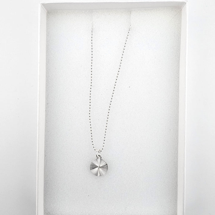 Sterling silver starburst disc necklace presented in a gift box on a white background.