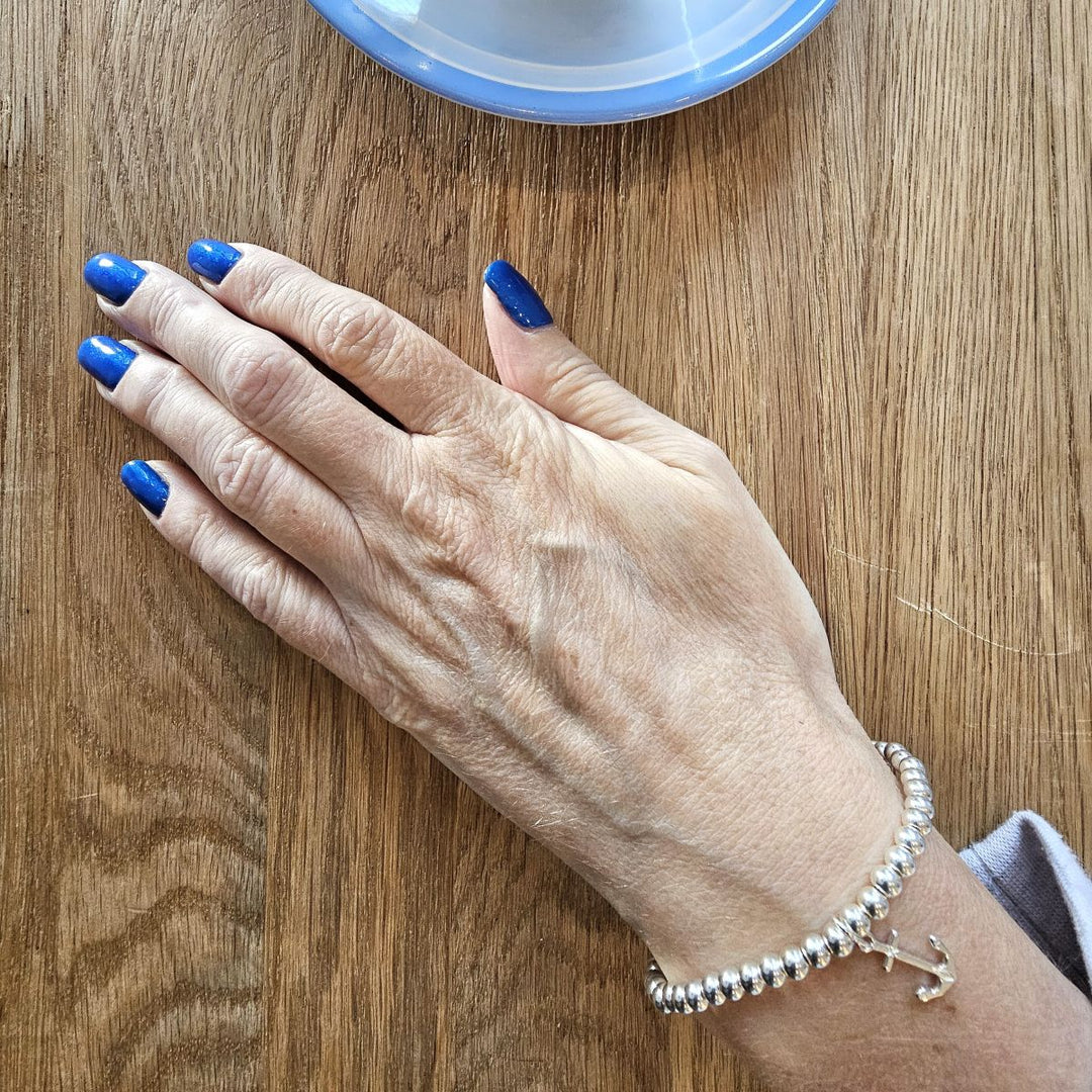 Sterling Silver Anchor bracelet from Bessie Bae worn on wrist while holding a blue cup on wooden table.