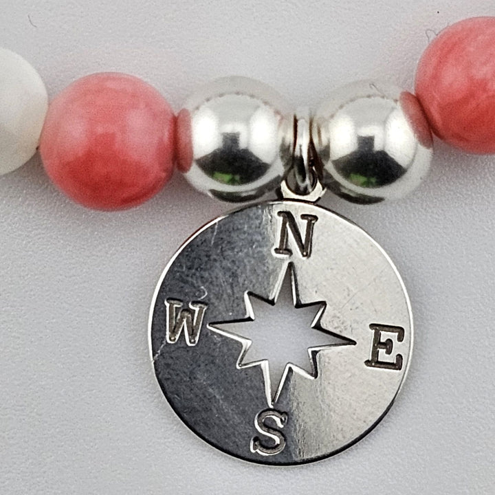 Close-up of compass charm engraved N E S W with silver and pearl beads.