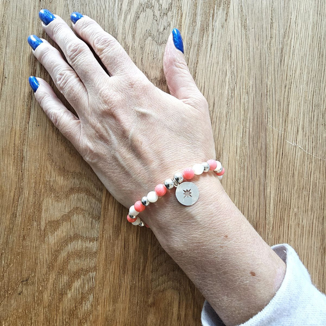 Sterling silver Compass and Mother of Pearl bracelet from Bessie Bae shown on wrist against wooden background.