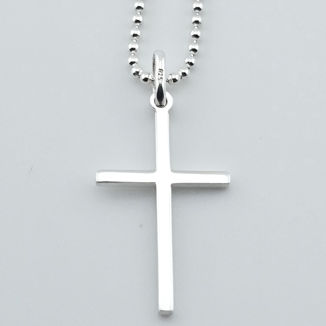 Close-up of sterling silver cross necklace, simple pendant on chain.