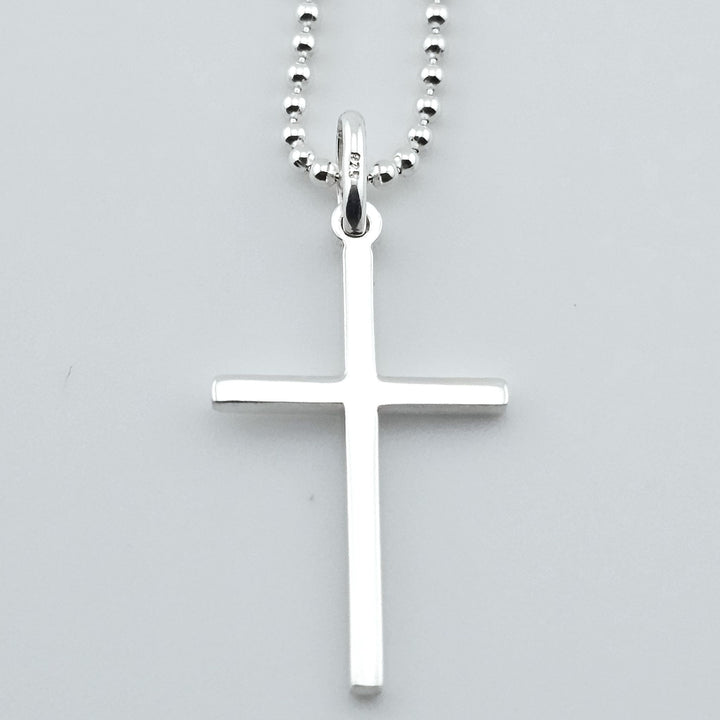 Close-up of sterling silver cross necklace, simple pendant on chain.