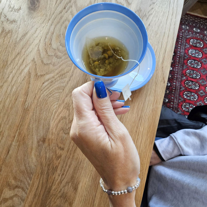 Sterling Silver Eye of Horus and Botswana Agate bracelet from Bessie Bae worn on wrist while holding a cup of tea.