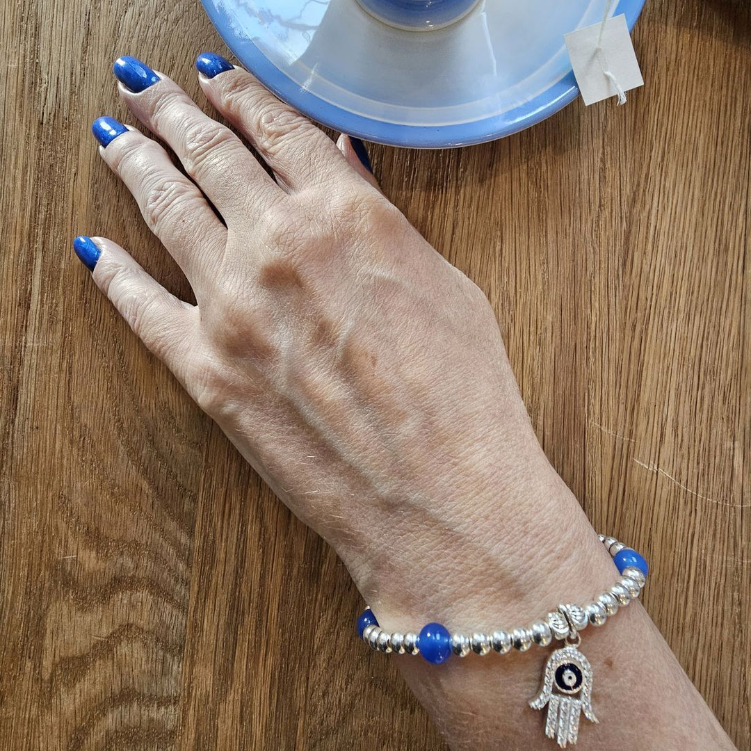 Sterling Silver Hamsa Hand bracelet with Blue Agate and Evil Eye charm from Bessie Bae shown on wrist while holding a blue cup.