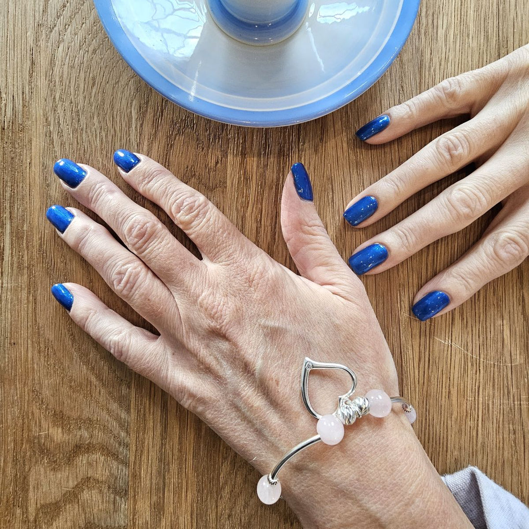 Rose quartz and sterling silver bracelet with open heart charm, worn on wrist beside a glass paperweight.