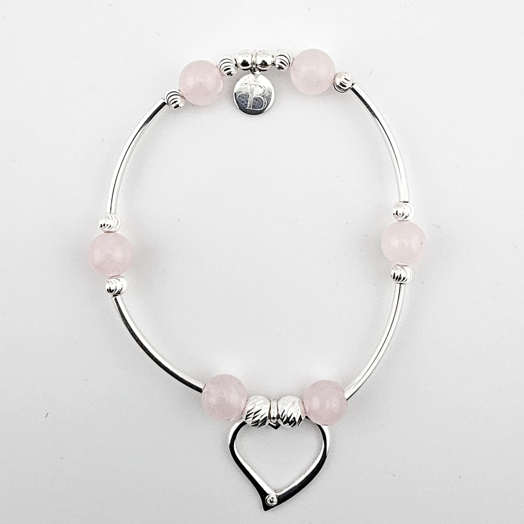 Sterling silver bracelet with rose quartz beads and open heart charm on white background.