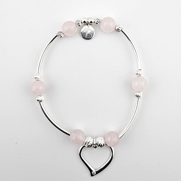 Sterling silver bracelet with rose quartz beads and open heart charm on white background.