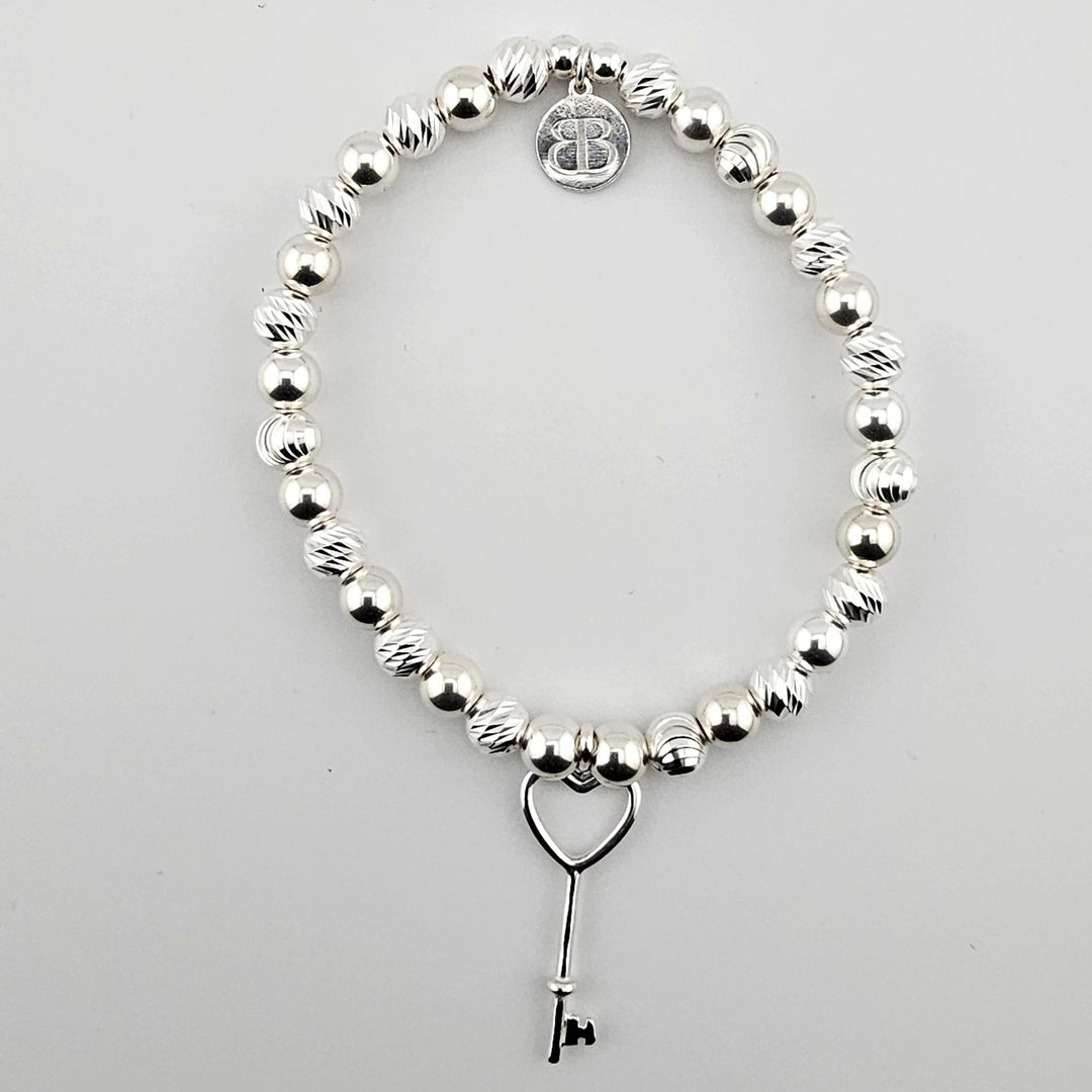 Sterling silver beaded bracelet with heart key charm on white background.