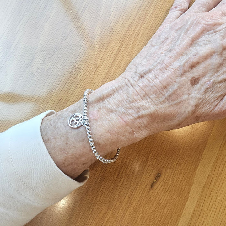 Sterling Silver Om Symbol Bracelet by Bessie Bae, featuring polished silver beads and a delicate Om charm, shown on wrist.