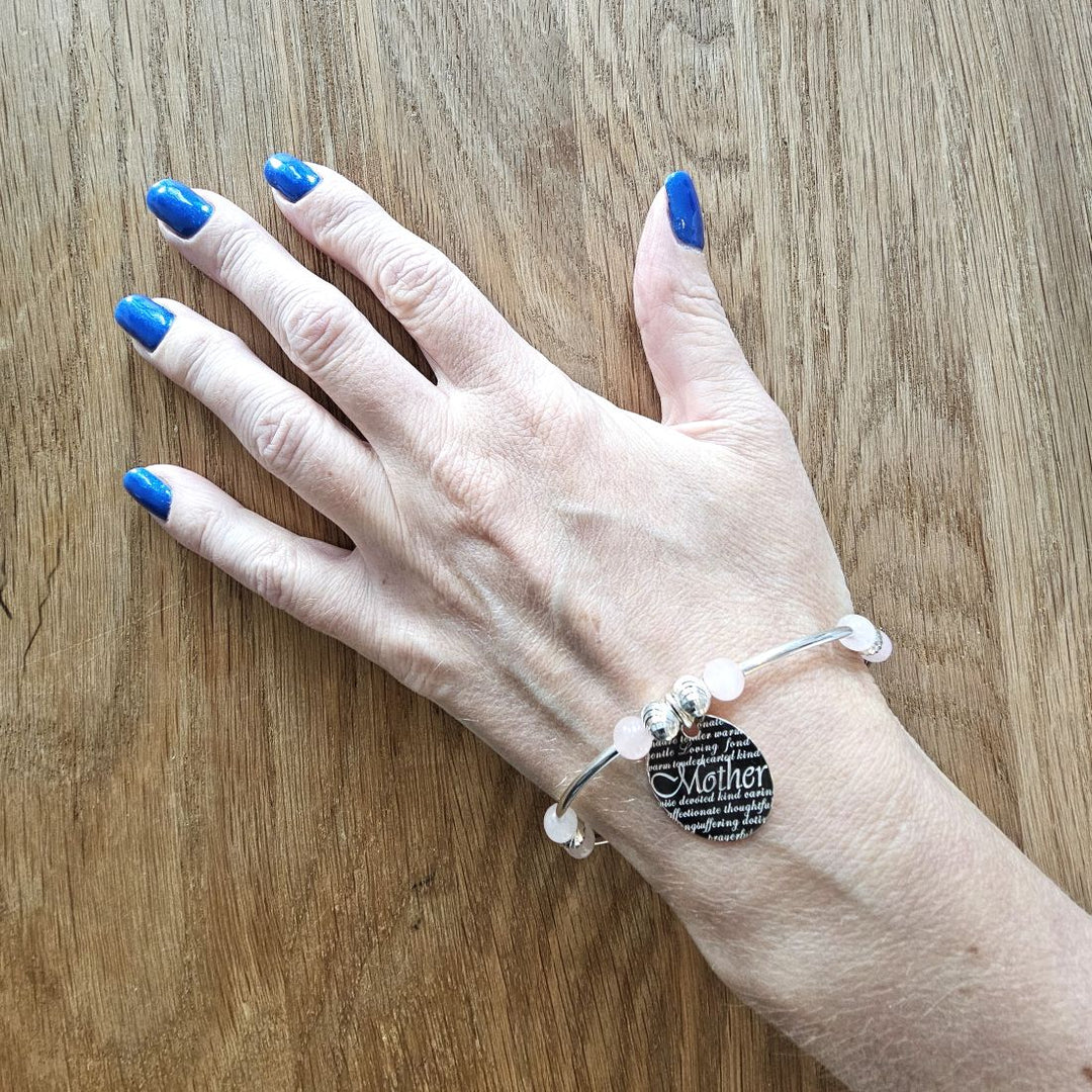 Sterling silver and rose quartz Mother bracelet from Bessie Bae shown on wrist against wooden background.