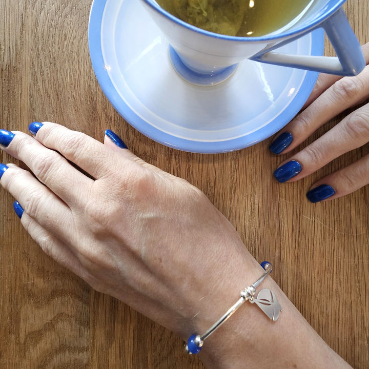 Sterling Silver Anchor bracelet from Bessie Bae worn on wrist while holding a blue cup on wooden table.