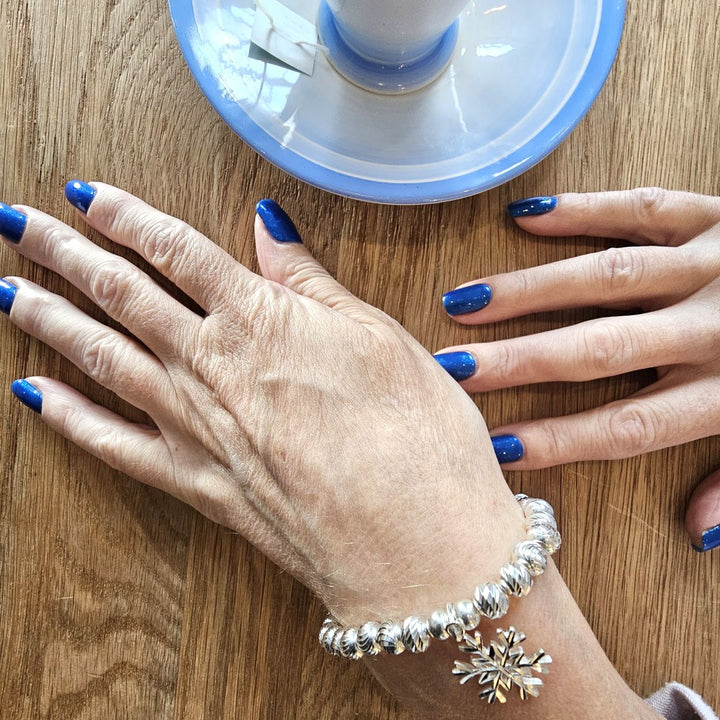 Sterling Silver Snowflake bracelet from Bessie Bae worn on wrist while holding a blue cup on wooden table.