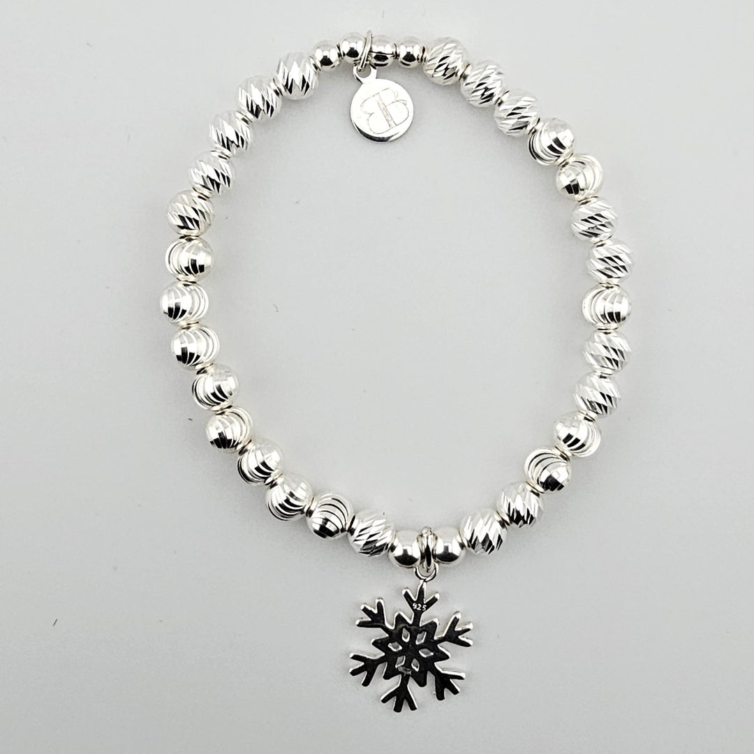 Sterling silver beaded bracelet with snowflake charm on white background.