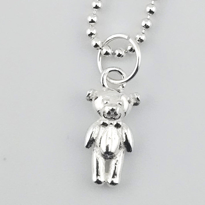 Close-up of a sterling silver teddy bear pendant showing polished detail and finish.