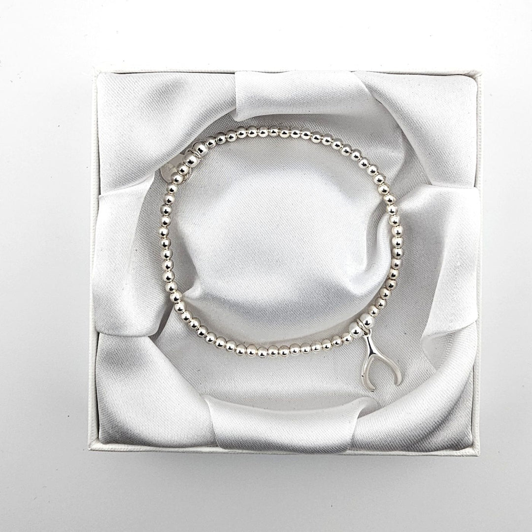Minimalist sterling silver beaded bracelet with wishbone charm in white box.