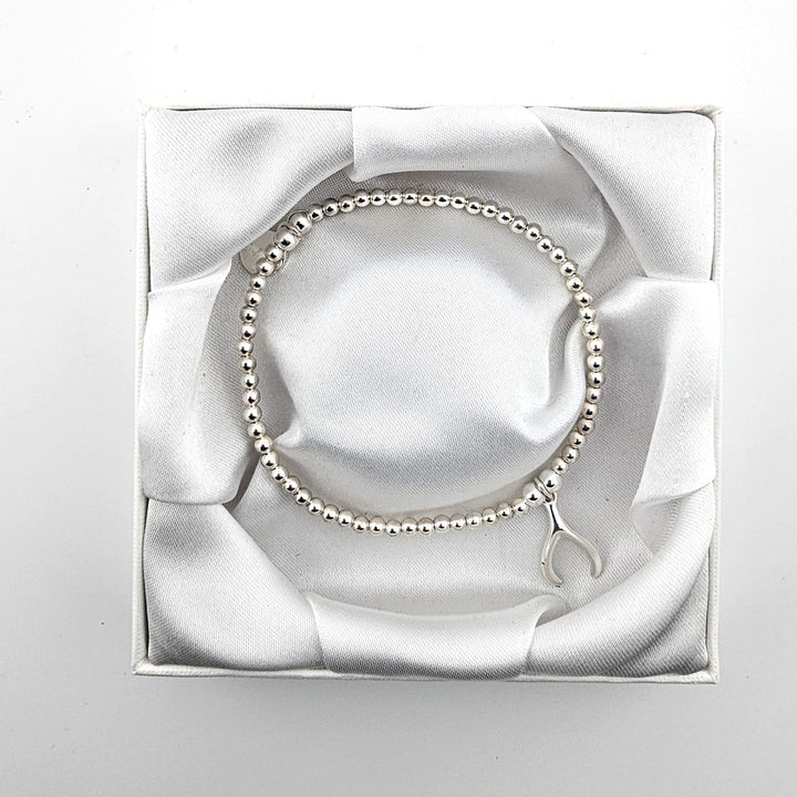 Minimalist sterling silver beaded bracelet with wishbone charm in white box.