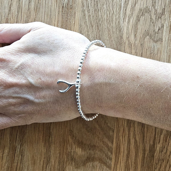 Sterling silver wishbone bracelet from Bessie Bae shown on wrist on wooden background.