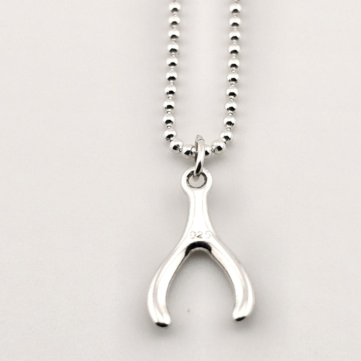Close-up of sterling silver wishbone necklace, minimalist lucky pendant.