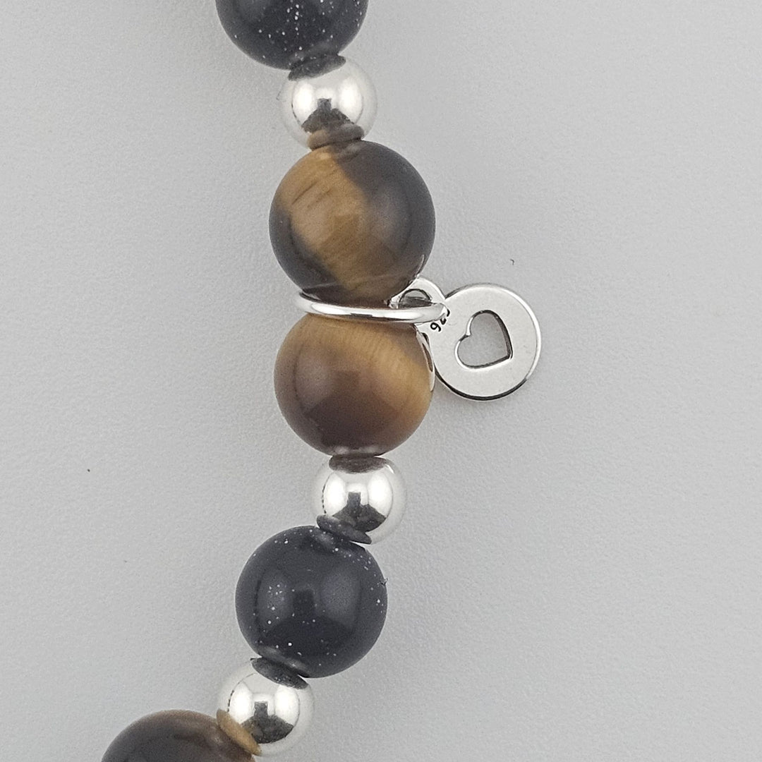 Macro detail of Tiger’s Eye and Goldstone beads with Sterling Silver accents and heart tag.