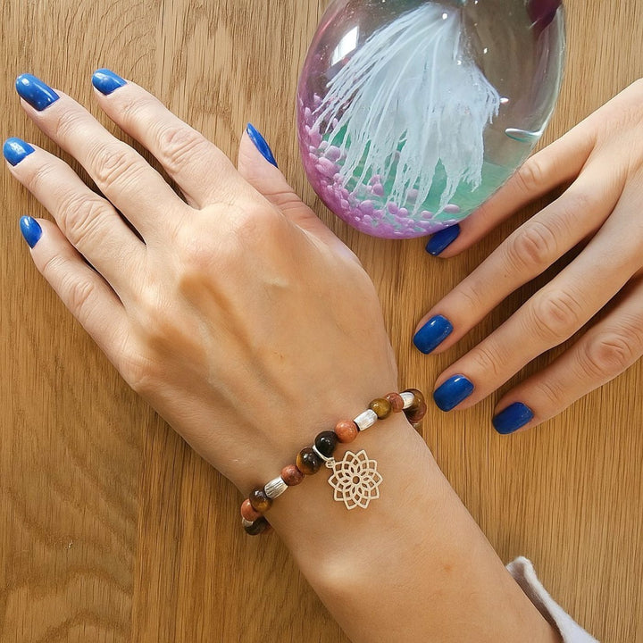 Tiger’s Eye and Goldstone bracelet with sterling silver lotus charm, shown on wrist beside a glass paperweight.